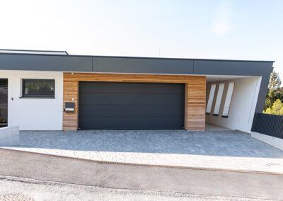 Garage mit Garagentor geschlossen, Farbe: schwarz, Ansicht von vorne auf Haus mit geschlossenem Garagentor, Aufnahme im Freien bei Sonnenschein