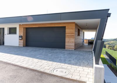 Garage mit Garagentor geschlossen, Farbe: schwarz, Ansicht schräg seiltich vorne auf Haus mit geschlossenem Garagentor, Aufnahme im Freien bei Sonnenschein