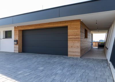Garage mit Garagentor geschlossen, Farbe: schwarz, Ansicht schräg seiltich vorne auf Haus mit geschlossenem Garagentor, Aufnahme im Freien bei Sonnenschein