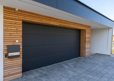Garagentor geschlossen, Farbe: schwarz, Ansicht schräg seiltich vorne auf Haus mit geschlossenem Garagentor, Aufnahme im Freien bei Sonnenschein