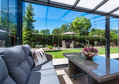 Terrassendach mit geschlossenen Glaselementen, Ansicht Terrassendach auf den Garten mit Gartenmöbeln
